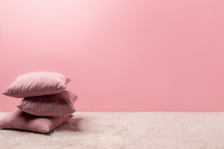 stack of pillows on carpet in front of pink wallの写真素材