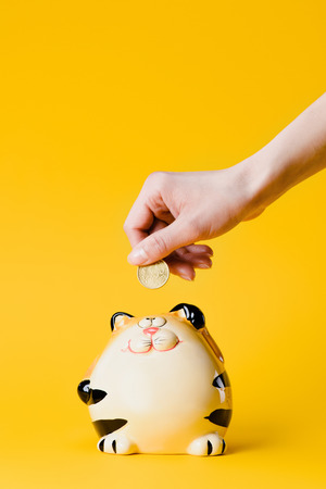 cropped shot of woman putting 50 euro cent into still bank isolated on yellowの写真素材