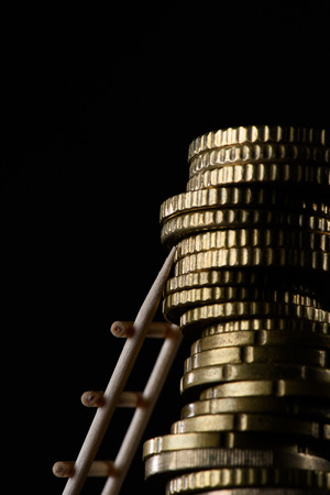 close up view of pile of coins with little wooden ladder isolated on blackの写真素材
