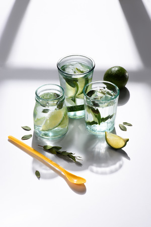 close up view of plastic spoon, glasses with water, lime pieces and ice cubes on white tabletopの写真素材