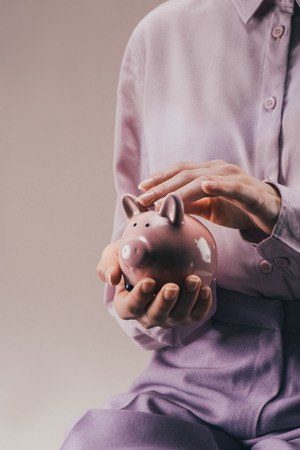 partial view of woman holding pink piggy bank in hands isolated on lilacの写真素材