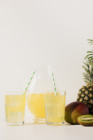 glasses with straws and glass jug with juice and fresh tropical fruits on grey の写真素材