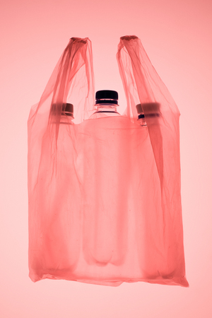 transparent plastic bag with plastic bottles under pastel pink toned lightの写真素材