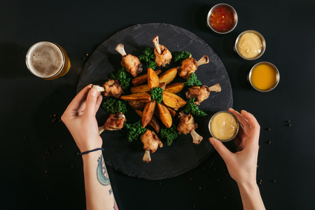 cropped shot of person eating tasty baked potatoes with fried chicken and sauces on blackの写真素材