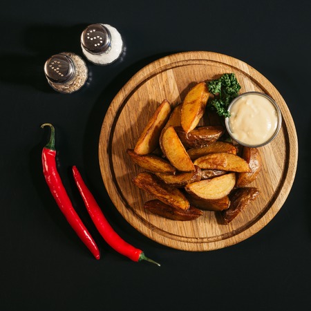delicious baked potatoes with sauce on wooden board, spices and chili peppers on black の写真素材