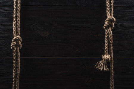 top view of arrangement of brown nautical ropes with knots on dark wooden tabletopの写真素材