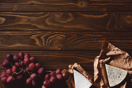 top view of slices of cheese on crumpled paper and ripe red grapes on wooden tableの写真素材