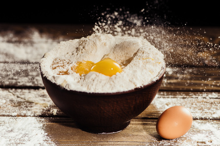yolks falling into bowl with flour on wooden table with one egg nearの写真素材