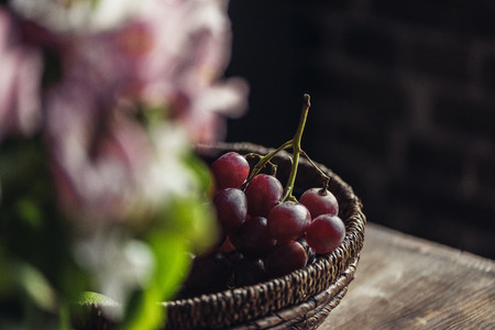 Close-up basket of red grapes on kitchen table and blurred flowers in foregroundの写真素材