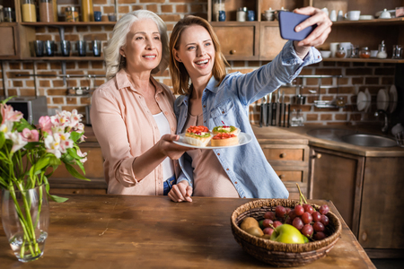 two women, senior and young taking selfie in kitchenの写真素材