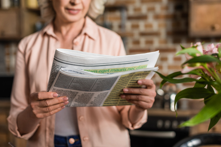 Portrait of senior woman reading newspaper during breakfast in kitchenの写真素材