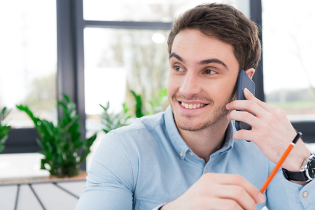 smiling businessman using smartphone in modern officeの写真素材