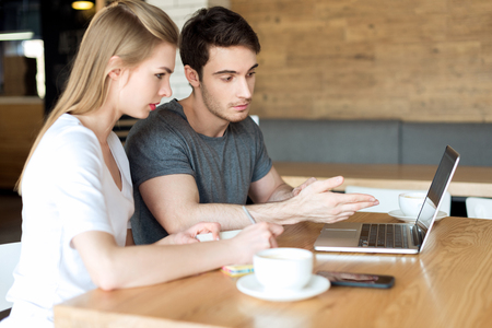 young couple working on laptop together while sitting at table in cafeの写真素材