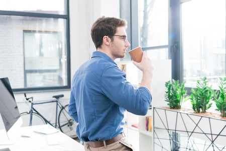 handsome businessman with disposable coffee cup in modern officeの写真素材