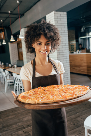 African american woman waitress bringing pizza for clients in cafeの写真素材