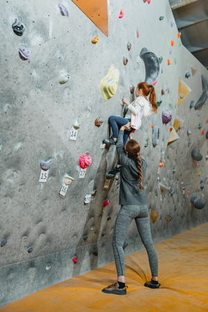 Full-length shot of little girl climbing a wall with grips and her mom supporting her from the groundの写真素材