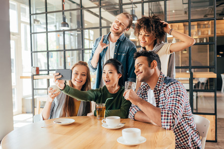 Young happy multiethnic friends taking selfie in cafeの写真素材