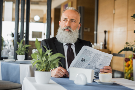 thoughtful businessman with newspaper in restaurant while waiting for meetingの写真素材