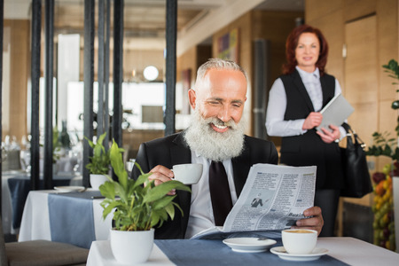 happy businessman reading newspaper in restaurant while waiting for meetingの写真素材