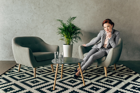 successful mature businesswoman resting on armchair in loft lobby interiorの写真素材