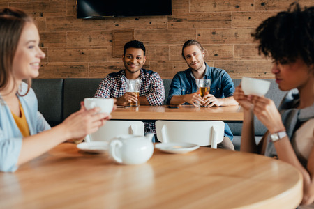 Two young men having beer and looking at women sitting at next table in cafeの写真素材