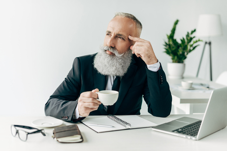 thoughtful senior businessman at workplace in modern officeの写真素材