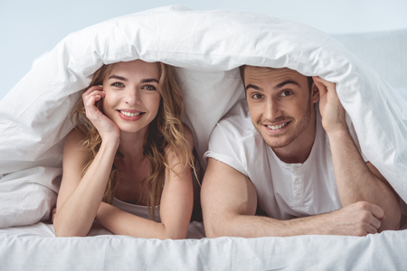young smiling couple and lying in bed and looking at cameraの写真素材