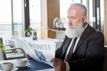 mature businessman reading newspaper in restaurant while waiting for meetingの写真素材