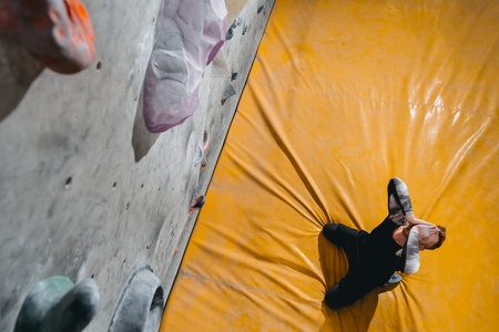 HIgh-angle shot of a man sitting on mat near a climbing wall, covering his face with hands in defeatの写真素材