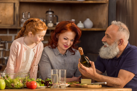 portrait of senior man and woman discussing bottle of wine while granddaughter standing near byの写真素材