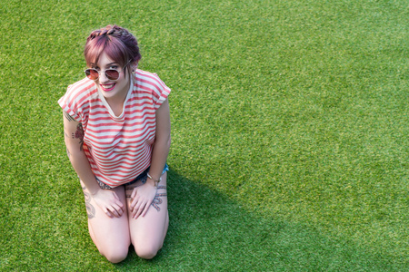 attractive young woman in sunglasses smiling at camera while kneeling on green grassの写真素材