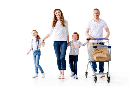 happy young family with two kids walking with shopping trolley isolated on whiteの写真素材