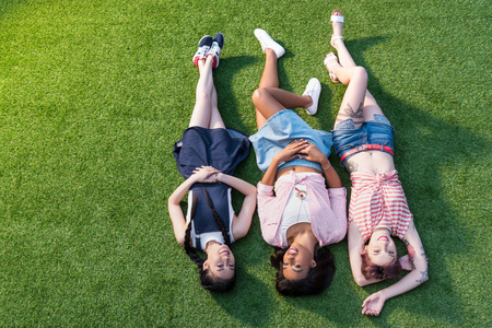 high angle view of happy young multiethnic women lying together on green grass の写真素材
