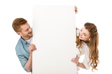 happy young couple holding blank placard and looking at copy space isolated on whiteの写真素材