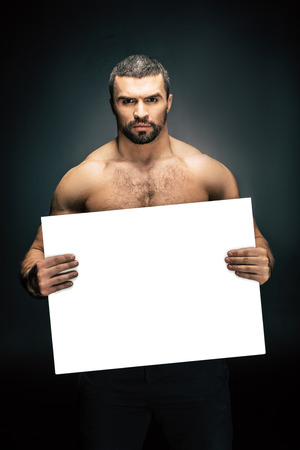 portrait of shirtless athletic man holding blank banner in hands isolated on blackの写真素材