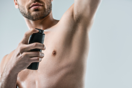cropped view of shirtless man spraying deodorant, isolated on greyの写真素材
