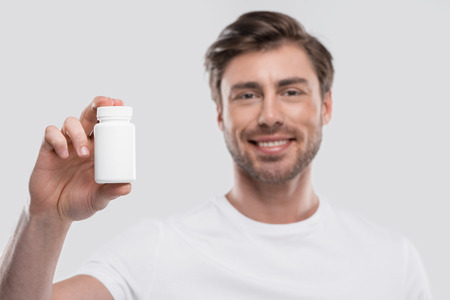 handsome man presenting vitamins in bottle, isolated on whiteの写真素材
