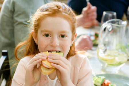 portrait of little girl looking at camera while eating sandwichの写真素材