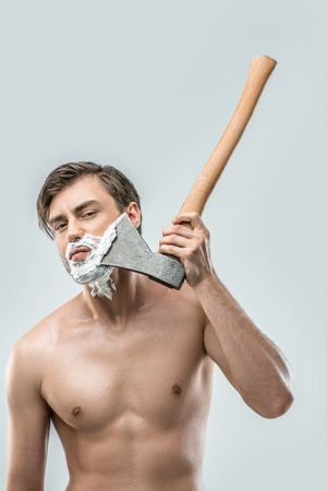 shirtless man in shaving foam shaving with ax, isolated on whiteの写真素材