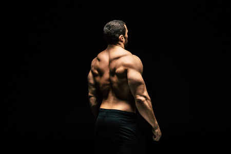 back view of shirtless sportive man showing muscles isolated on blackの写真素材