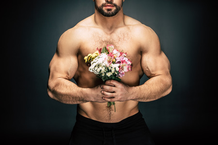 partial view of shirtless sportive man holding bouquet of flowers in hands isolated on blackの写真素材