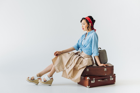 beautiful asian woman in retro clothes sitting on luggage isolated on greyの写真素材