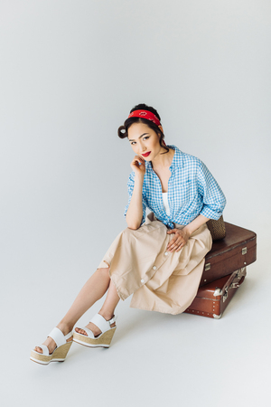 beautiful asian woman in retro clothes sitting on luggage isolated on greyの写真素材
