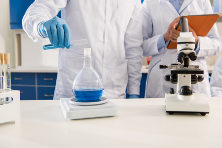 Partial view of medical worker pouring liquid from test tube into flask and weighing it on electronic scalesの写真素材