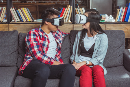 young couple in vr headsets looking at each other while sitting on sofaの写真素材
