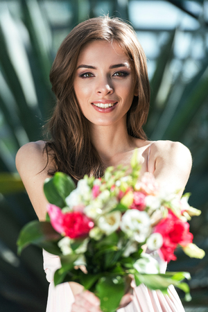 young smiling beautiful woman showing bouquet of flowersの写真素材