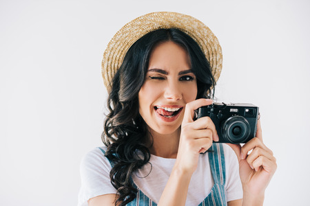 portrait of winking woman with photo camera in hands sticking tongue out isolated on greyの写真素材