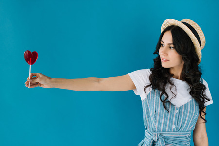 portrait of beautiful woman looking at lollipop in hand isolated on blue