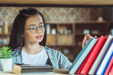 beautiful young student in eyeglasses choosing books in libraryの写真素材