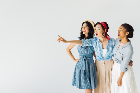 shocked multicultural women looking away while asian woman pointing at something  isolated on greyの写真素材